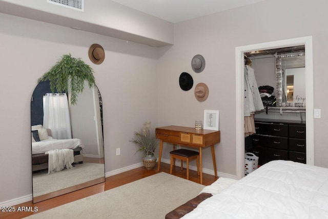 bedroom with baseboards, visible vents, wood finished floors, and a closet