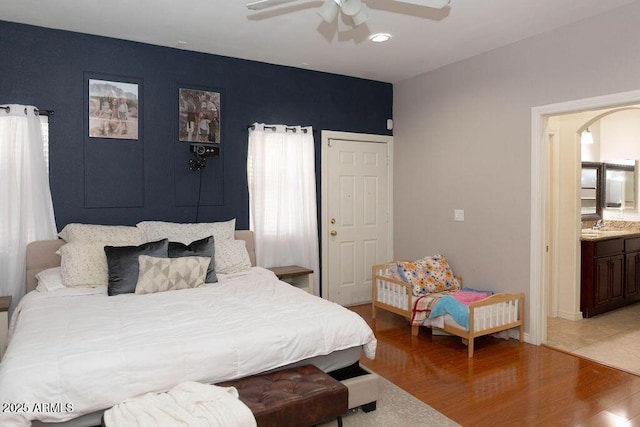 bedroom featuring arched walkways, a ceiling fan, ensuite bath, and light wood-style floors