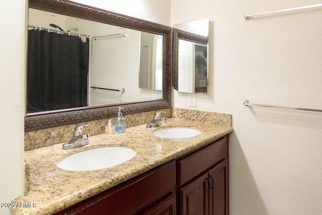 bathroom with a shower with shower curtain, double vanity, a textured wall, and a sink