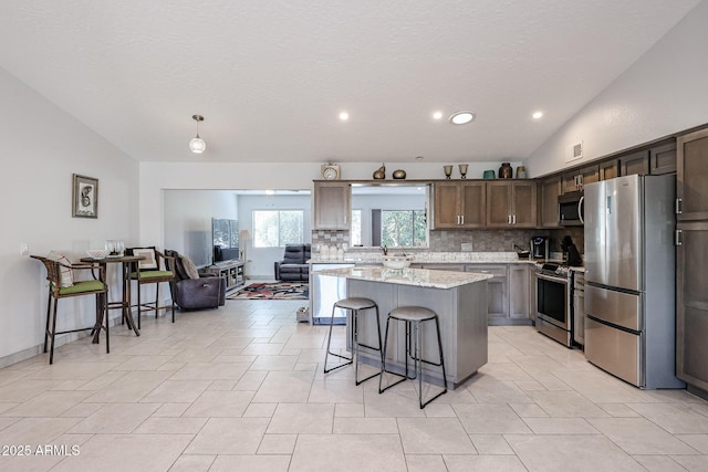 kitchen with stainless steel appliances, vaulted ceiling, decorative backsplash, a center island, and a kitchen bar