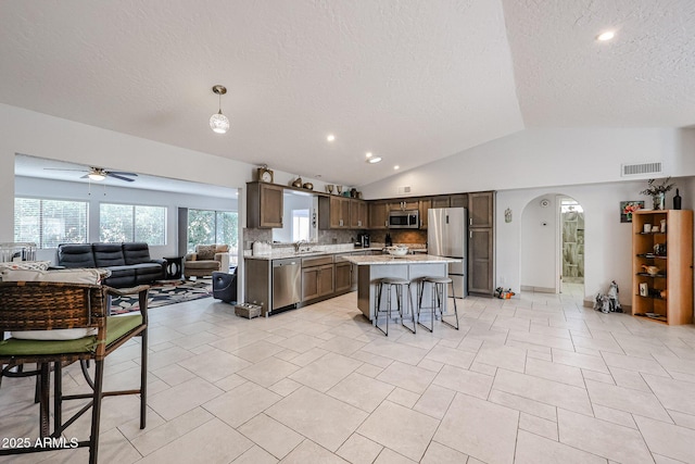 kitchen with arched walkways, stainless steel appliances, visible vents, a kitchen breakfast bar, and open floor plan