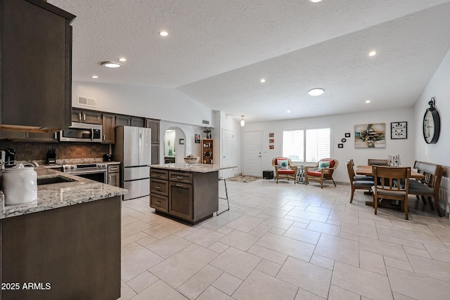 kitchen featuring arched walkways, appliances with stainless steel finishes, visible vents, and dark brown cabinetry