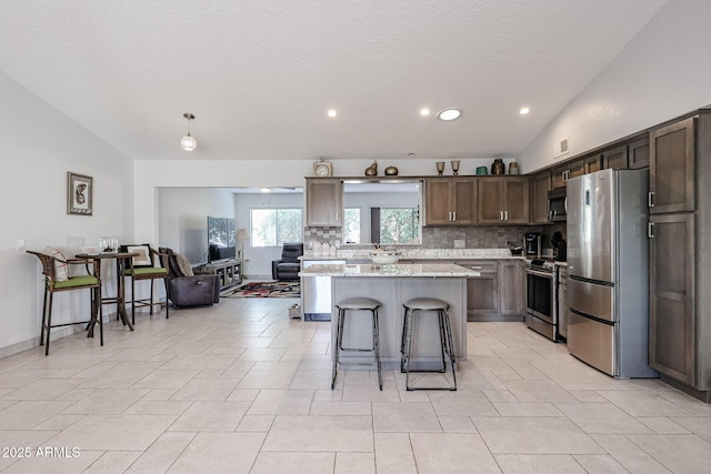 kitchen featuring tasteful backsplash, a breakfast bar area, a center island, vaulted ceiling, and stainless steel appliances