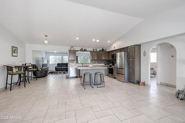 kitchen featuring a center island, arched walkways, a breakfast bar area, stainless steel appliances, and lofted ceiling