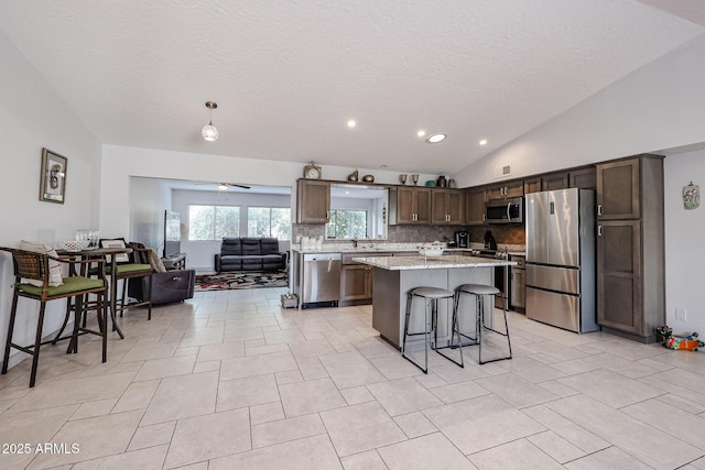 kitchen featuring dark brown cabinetry, vaulted ceiling, stainless steel appliances, and a kitchen breakfast bar