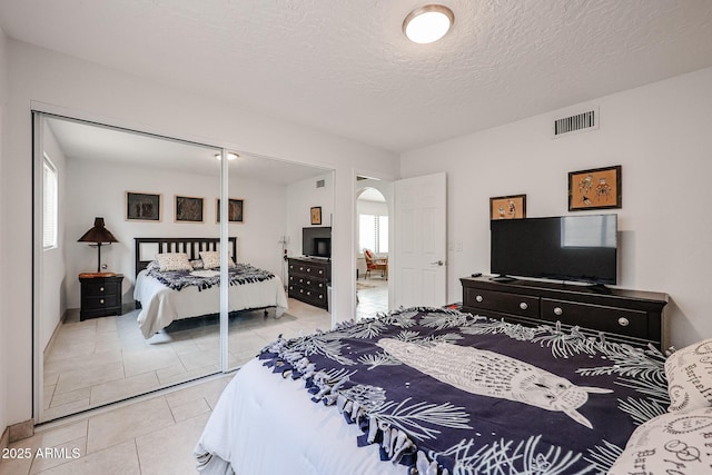 tiled bedroom with arched walkways, a closet, visible vents, and multiple windows