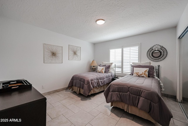 bedroom featuring a textured ceiling, light tile patterned flooring, and baseboards