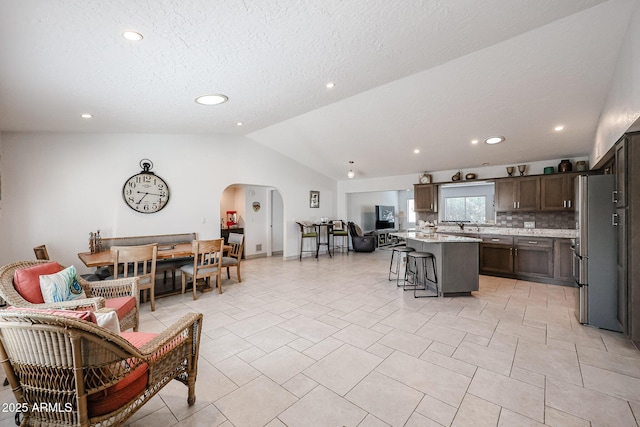 kitchen with arched walkways, a breakfast bar, freestanding refrigerator, vaulted ceiling, and light countertops