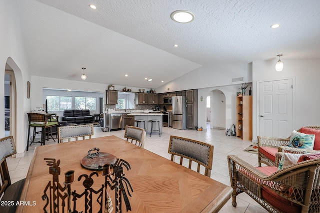 dining space with arched walkways, visible vents, light tile patterned flooring, vaulted ceiling, and a textured ceiling