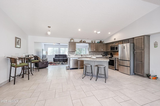 kitchen with a breakfast bar, appliances with stainless steel finishes, open floor plan, vaulted ceiling, and a kitchen island