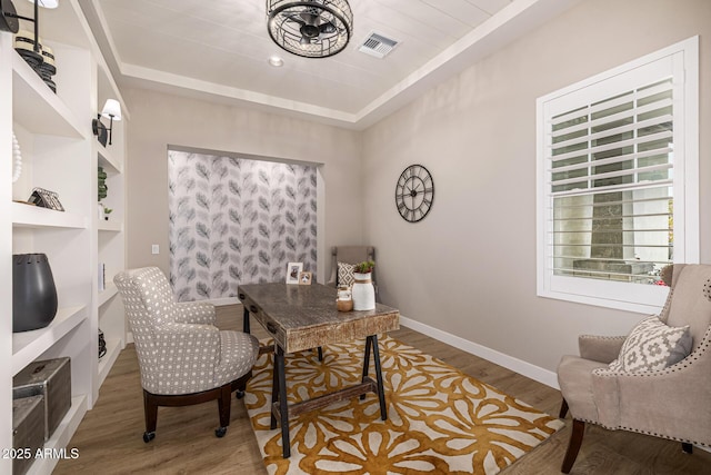 home office with visible vents, a raised ceiling, baseboards, and wood finished floors