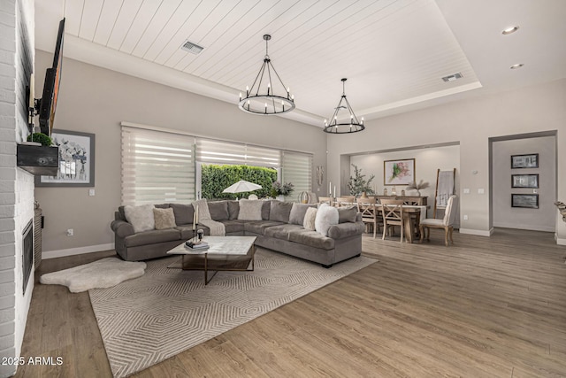 living room with visible vents, baseboards, a fireplace, wood finished floors, and a raised ceiling