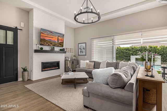 living room with a notable chandelier, wood finished floors, a barn door, a fireplace, and a raised ceiling