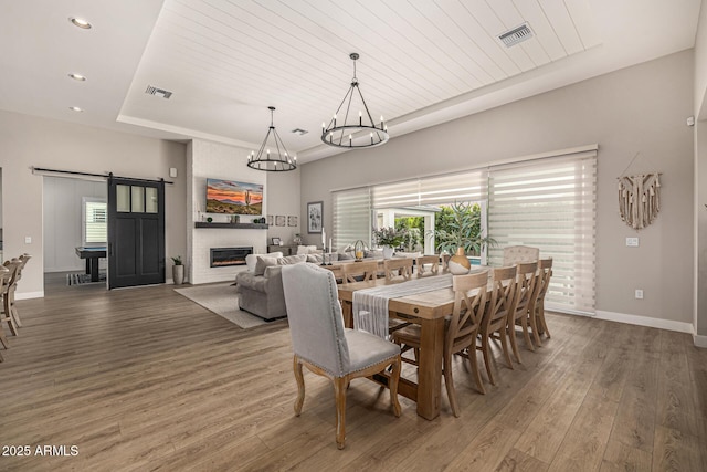 dining room featuring a tray ceiling, a barn door, visible vents, and wood finished floors