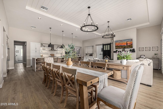 dining space featuring a tray ceiling, a notable chandelier, visible vents, and light wood finished floors