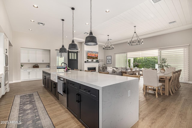 kitchen with visible vents, light wood-type flooring, a lit fireplace, a large island with sink, and a sink