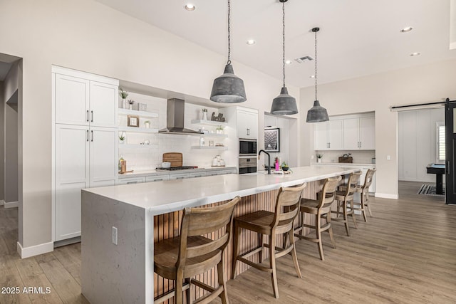 kitchen with visible vents, a barn door, appliances with stainless steel finishes, wall chimney exhaust hood, and open shelves