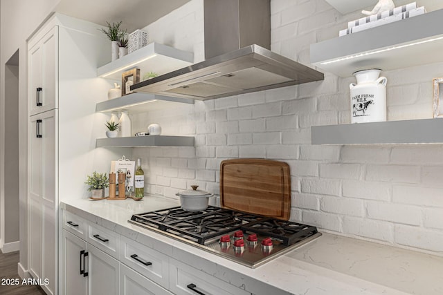 kitchen featuring tasteful backsplash, stainless steel gas stovetop, white cabinetry, wall chimney exhaust hood, and open shelves