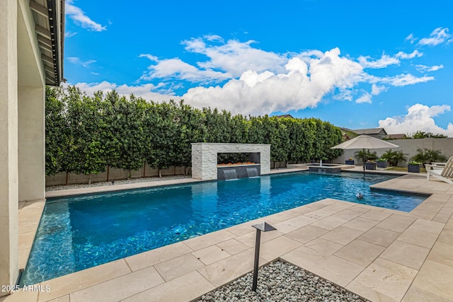 view of swimming pool with a patio, a lit fireplace, a fenced backyard, and a pool with connected hot tub