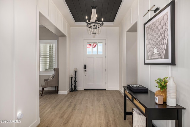 entrance foyer featuring light wood-type flooring, baseboards, an inviting chandelier, and wooden ceiling