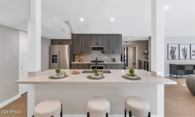 kitchen featuring a kitchen breakfast bar, stainless steel appliances, sink, dark brown cabinetry, and light hardwood / wood-style floors