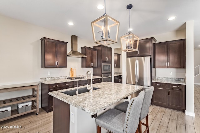 kitchen with wall chimney exhaust hood, stainless steel appliances, a sink, dark brown cabinets, and a breakfast bar