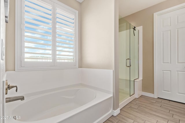 full bathroom with a shower stall, a bath, wood finished floors, and baseboards