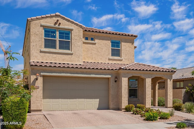 mediterranean / spanish-style house featuring an attached garage, decorative driveway, stucco siding, and a tiled roof