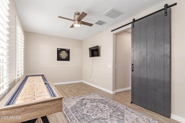 game room with a barn door, ceiling fan, light wood finished floors, and plenty of natural light