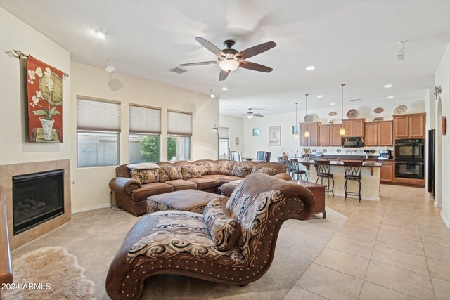 living room with ceiling fan, light tile patterned flooring, and a tiled fireplace