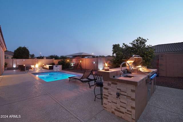 pool at dusk with a patio, an outdoor bar, and exterior kitchen