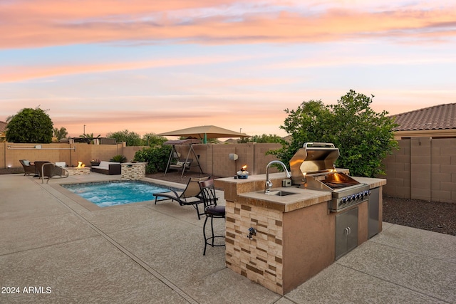 pool at dusk featuring a patio area, an outdoor kitchen, and a wet bar