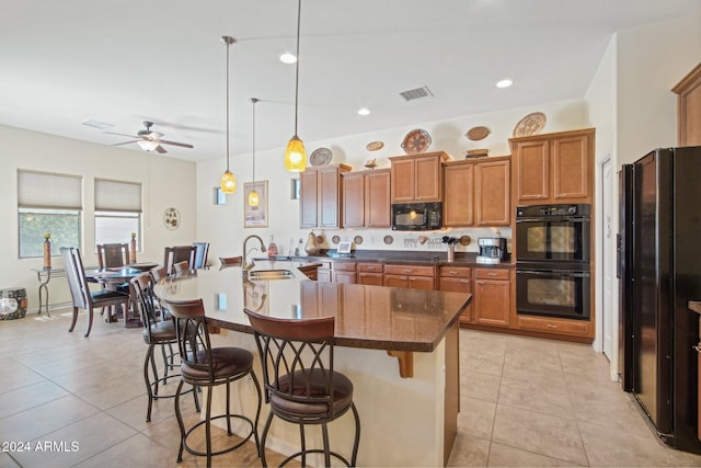 kitchen featuring sink, pendant lighting, a breakfast bar, black appliances, and a center island with sink