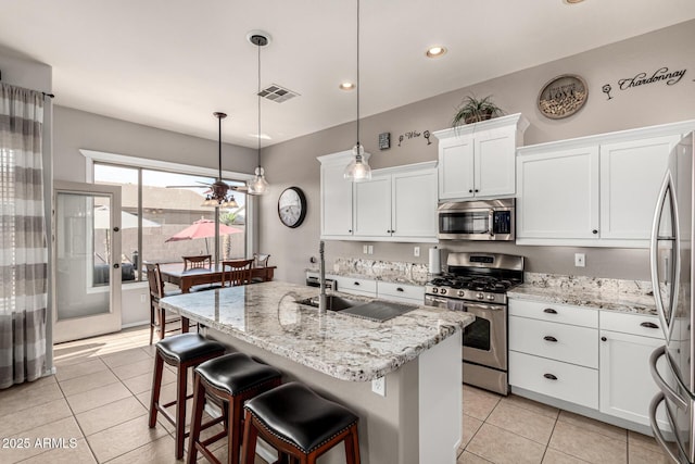 kitchen with appliances with stainless steel finishes, light tile patterned floors, a sink, white cabinets, and light stone countertops