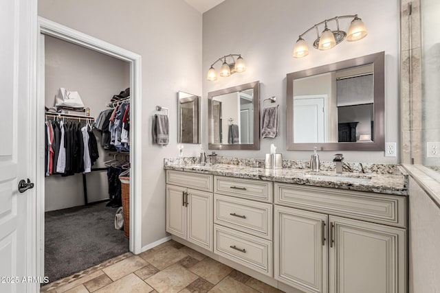 full bathroom featuring double vanity, stone finish flooring, a spacious closet, and baseboards