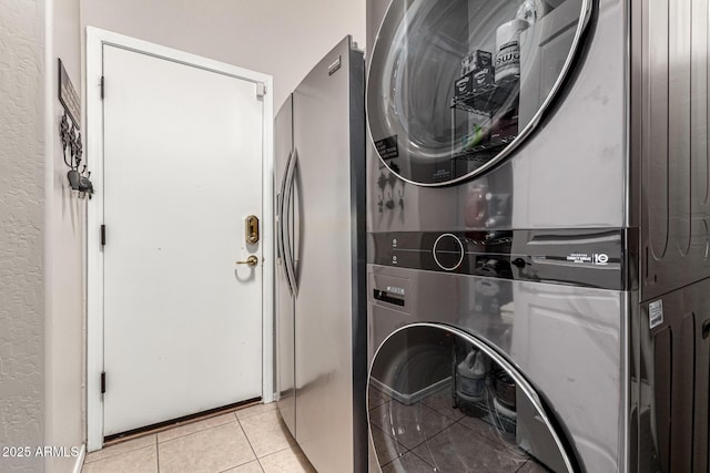 laundry area with stacked washer / dryer, light tile patterned flooring, and a textured wall