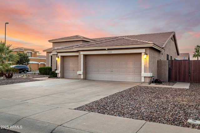 view of front facade with an attached garage, driveway, fence, stucco siding, and a tiled roof