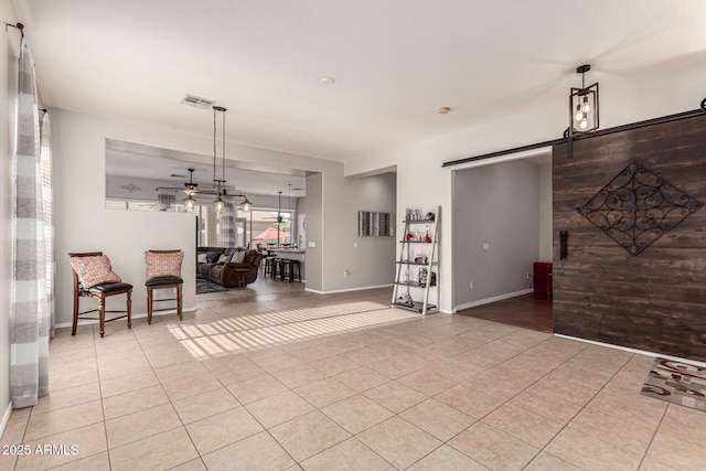 living area featuring a barn door, light tile patterned floors, a ceiling fan, and baseboards