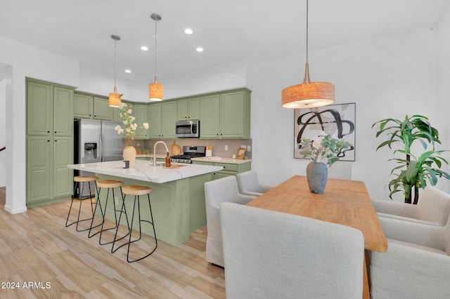 kitchen featuring stainless steel appliances, light hardwood / wood-style floors, green cabinets, tasteful backsplash, and decorative light fixtures