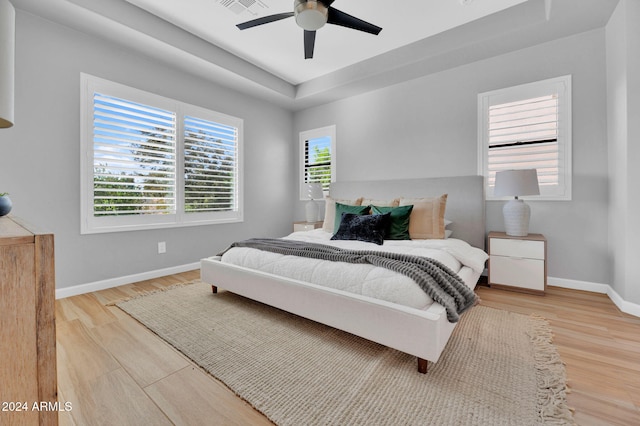 bedroom with ceiling fan, wood-type flooring, and a raised ceiling