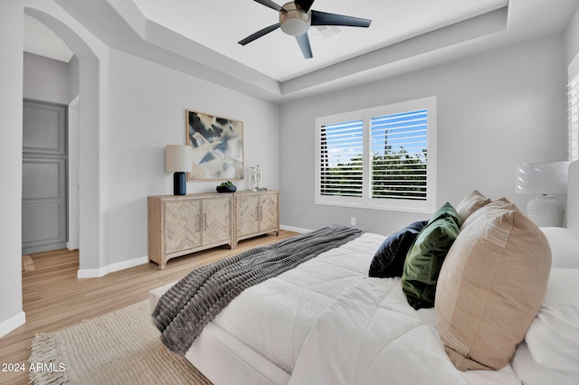 bedroom featuring a tray ceiling, light hardwood / wood-style floors, and ceiling fan