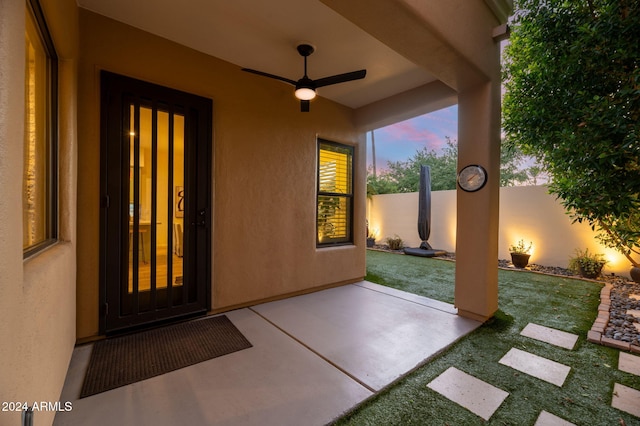 patio terrace at dusk featuring ceiling fan and a yard