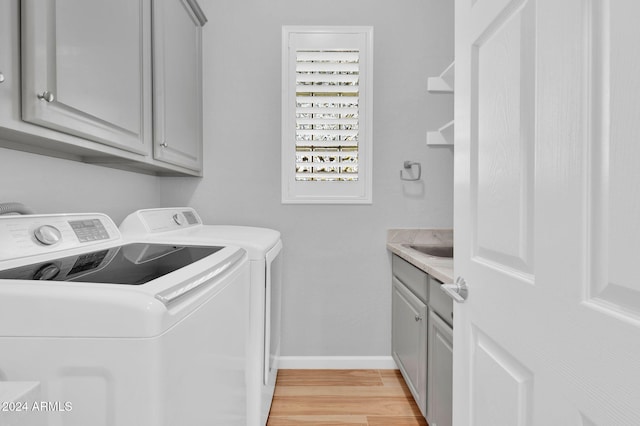 washroom featuring cabinets, washing machine and dryer, sink, and light hardwood / wood-style flooring