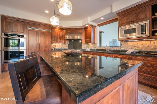 kitchen with hanging light fixtures, stainless steel appliances, dark stone countertops, extractor fan, and a kitchen island