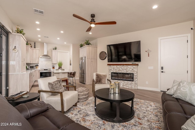 living room featuring ceiling fan, a stone fireplace, and light hardwood / wood-style floors