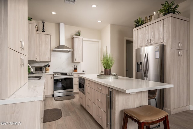 kitchen featuring appliances with stainless steel finishes, a center island, wall chimney range hood, a kitchen breakfast bar, and light wood-type flooring