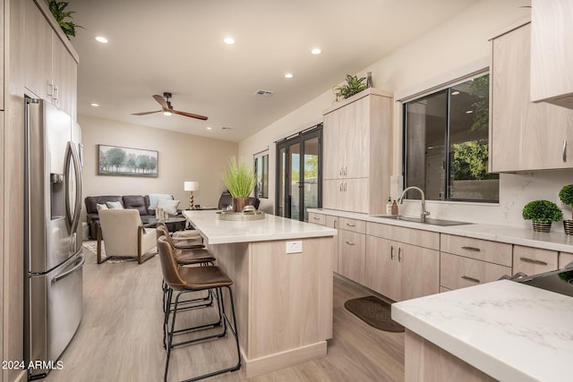 kitchen with a kitchen island, stainless steel refrigerator with ice dispenser, light brown cabinetry, a breakfast bar, and light hardwood / wood-style flooring