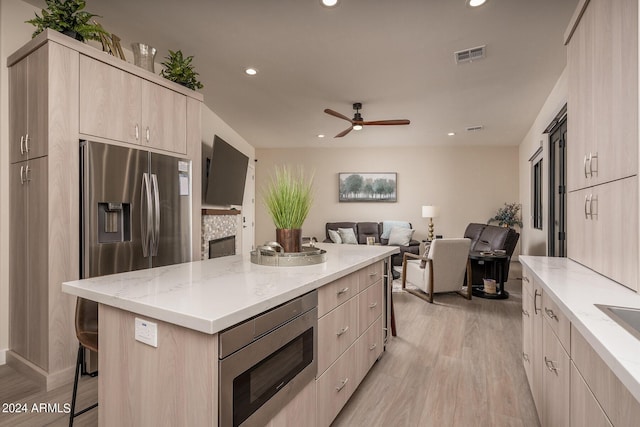 kitchen featuring a kitchen breakfast bar, light brown cabinets, appliances with stainless steel finishes, light wood-type flooring, and a center island