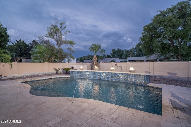 pool at dusk with pool water feature and a patio