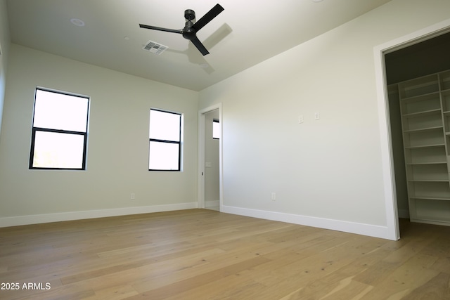 unfurnished bedroom featuring ceiling fan, a spacious closet, light hardwood / wood-style floors, and a closet